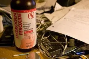 Bottle of hydrogen peroxide topical solution surrounded by medical supplies and cables on a wooden