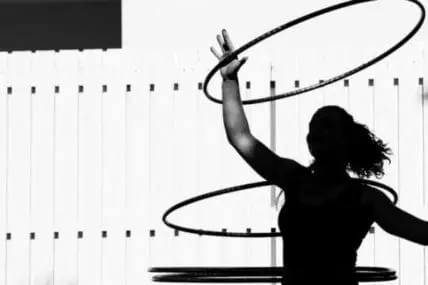 Woman silhouette hula hooping indoors against white wall