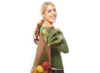 Woman holding fresh vegetables and greens in a mesh bag