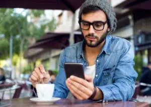 Man using smartphone at outdoor café while holding coffee cup