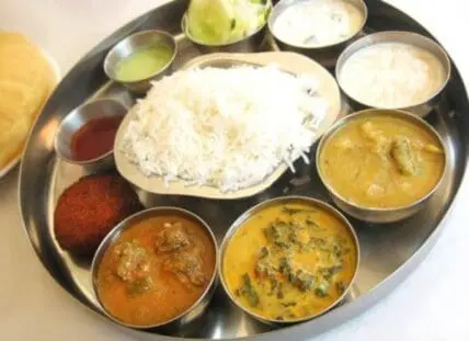 Indian vegetarian thali with rice, breads, and curries in metal bowls