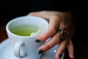 Woman holding a white mug of green tea with manicured nails
