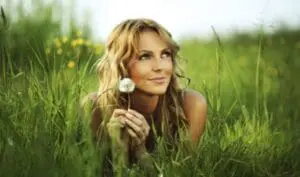 Woman in a green field holding a dandelion flower