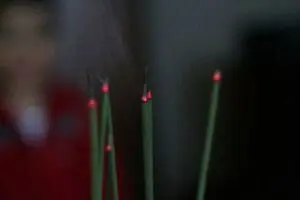 Lit incense sticks with glowing red tips against a dark background