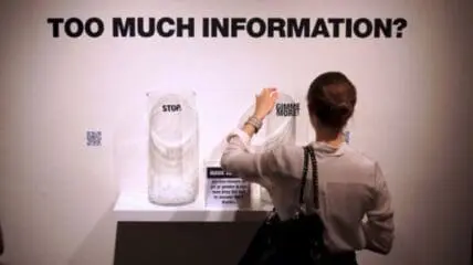 Person viewing an interactive art installation with "STOP" and "GIMME MORE" signs exploring
