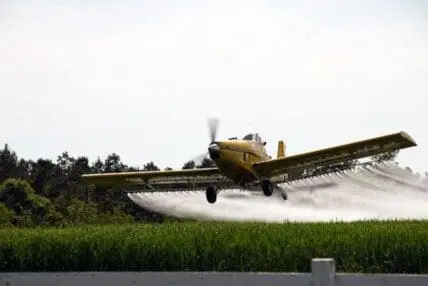 Crop duster plane spraying pesticide over agricultural field