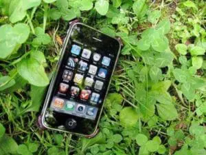 Black iPhone displaying home screen on grass and clover ground cover
