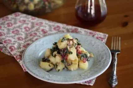 Creamy potato salad with beets and greens on a decorative white plate