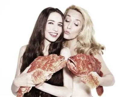Two women posing together while holding large red fish against their bodies