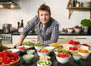 Man in plaid shirt surrounded by fresh vegetables and ingredients in a kitchen.