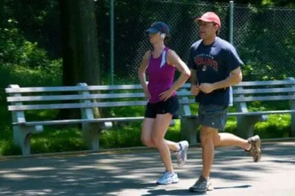Two people jogging together on a wooden boardwalk surrounded by green trees