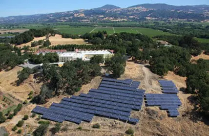 Aerial view of a solar panel array in a rural valley with mountains and a large building in the