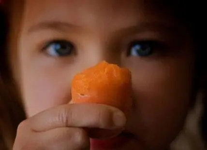 Child holding a peeled orange up to face