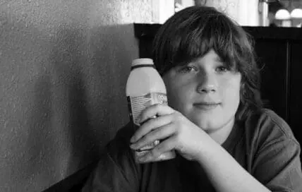 Young child holding a plastic bottle against textured wall in black and white photograph