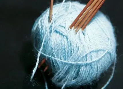 Light blue yarn ball with wooden knitting needles on dark background