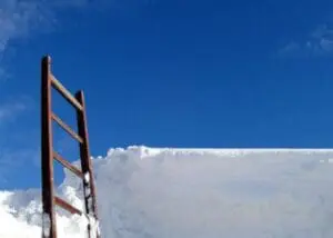 Rusty ladder leaning against a white wall with blue sky above