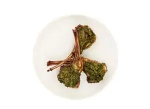Herb-crusted lamb chops with pesto on a white plate