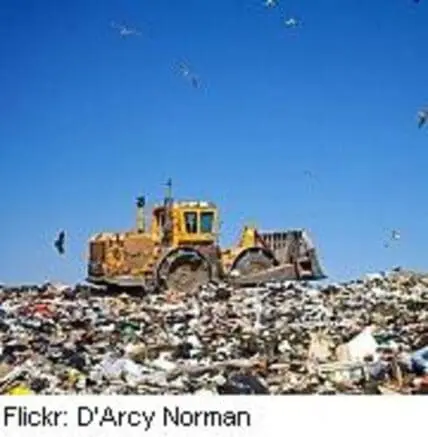 Large yellow bulldozer compacting waste at a landfill under clear blue sky