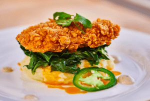 Crispy breaded chicken cutlet with greens and jalapeño slices on white plate