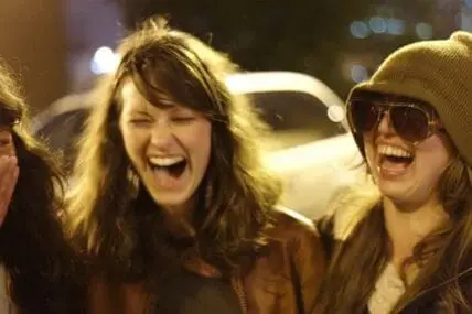Three women laughing together outdoors at night