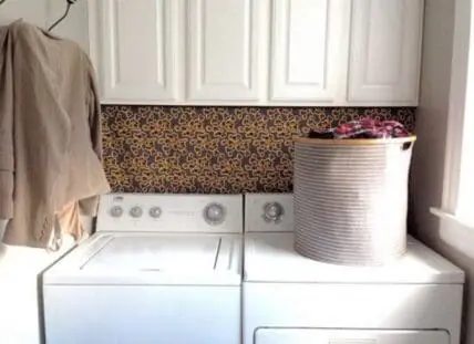 White washer and dryer with laundry basket in a utility room with patterned backsplash
