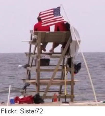 Lifeguard tower on beach with American flag and calm ocean water visible in background