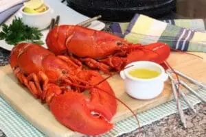Cooked lobsters on a wooden board with melted butter and serving utensils