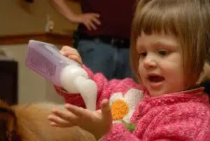 Toddler applying moisturizer lotion to skin while wearing pink sweater