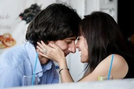A couple leaning close together and smiling at each other across a table
