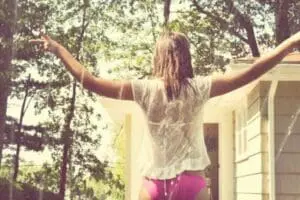 Woman with arms raised outdoors in front of a house surrounded by trees