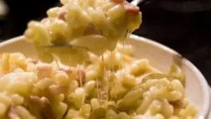 Creamy mac and cheese being lifted on a fork with melted cheese stretching from the plate