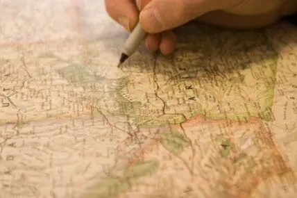 Hand pointing to a location on a vintage map with a pen
