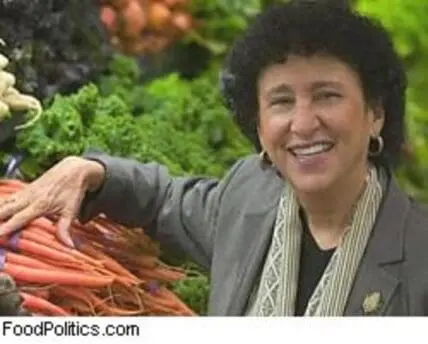Marion Nestle smiling while holding fresh carrots in a garden