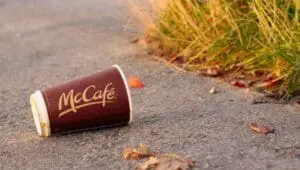 Discarded McCafé coffee cup on pavement beside grass
