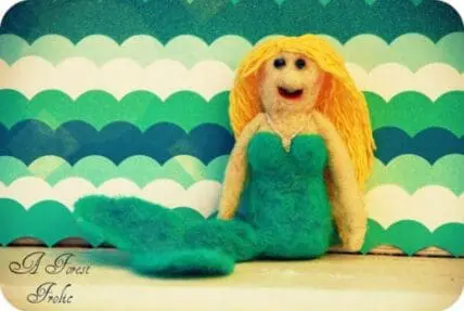Handmade felt mermaid craft with yellow hair against striped ocean backdrop