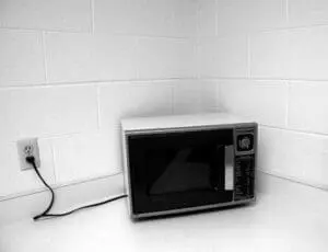 Vintage microwave oven plugged in against white tiled wall