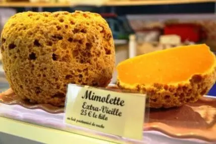 Mimolette cheese wheel cut in half displaying bright orange interior and porous texture with price