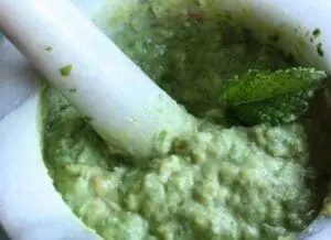 Mortar and pestle grinding fresh mint and green ingredients into a vibrant green chutney paste