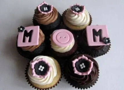 Homemade cupcakes decorated with pink fondant squares and floral toppers arranged for Mother's Day