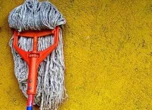 Mop with red handle leaning against bright yellow wall
