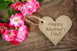 Pink roses with wooden heart-shaped tag reading "Happy Mother's Day" on rustic wood surface