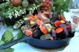 Cast-iron skillet of roasted mussels and clams with fresh vegetables in background