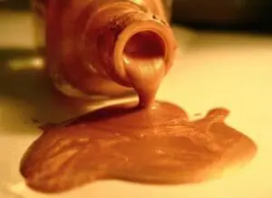 Copper-colored nail polish pouring from a bottle onto a surface
