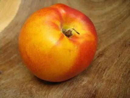 A ripe nectarine with red and yellow skin on a wooden surface