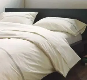 Unmade bed with white linens and pillows against a dark headboard
