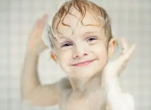 Young child washing face with soap and water in shower