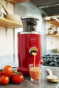 Red Novis Vita juicer dispensing fresh tomato juice into a glass on a kitchen counter