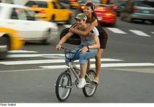 Two people riding a bicycle together on a busy New York City street