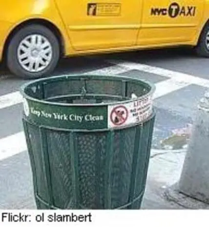 Green NYC street trash bin with "Keep New York City Clean" label and taxi in background