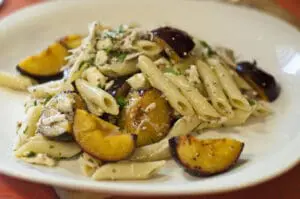 Pesto pasta with roasted stone fruit and almonds on a white plate